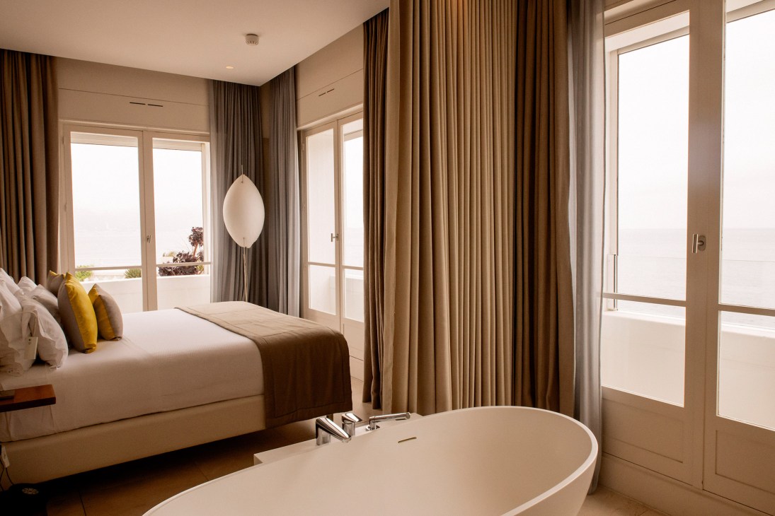 Luxury hotel bedroom with ocean views, modern furnishings, and floor-to-ceiling windows overlooking the Mediterranean.