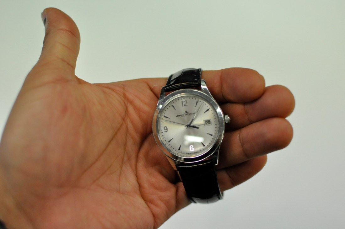 Hand holding a Jaeger-LeCoultre watch with silver dial and black leather strap.