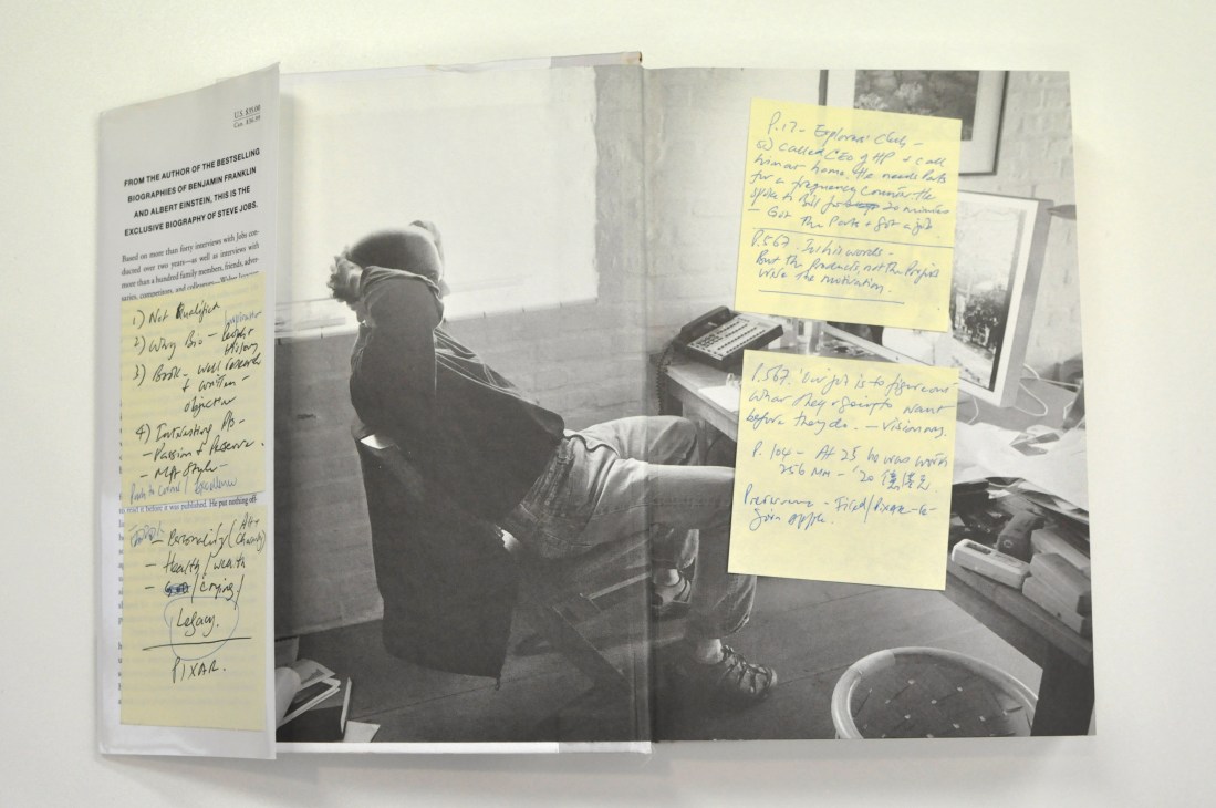 Open book with Steve Jobs biography and handwritten yellow sticky notes on pages.