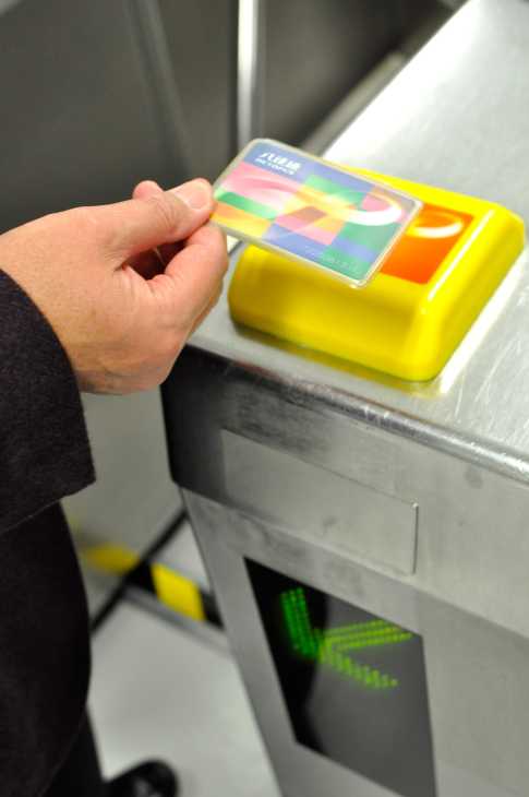 Hand holding a colorful Octopus card above a yellow MTR reader device.