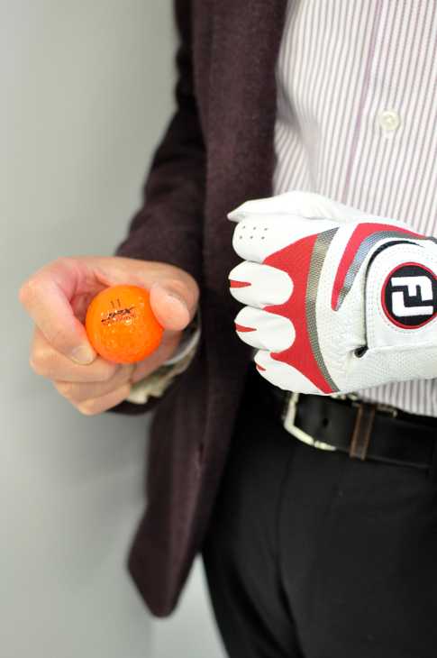 Man in golf glove holding an orange ball