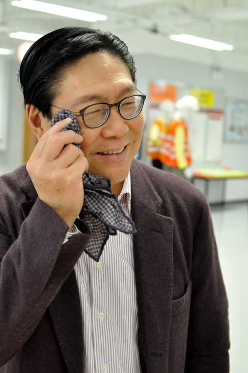 Man in glasses and brown jacket smiling while on a phone call.