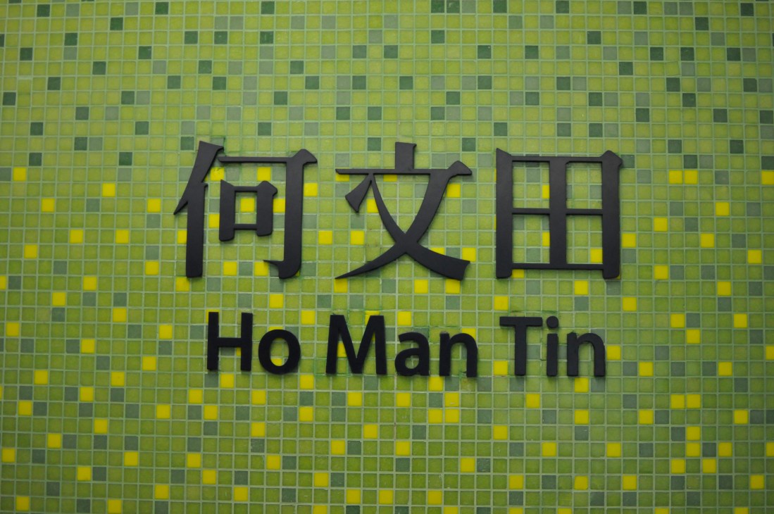 Ho Man Tin MTR station sign with Chinese characters and English text on yellow and green tiled wall.