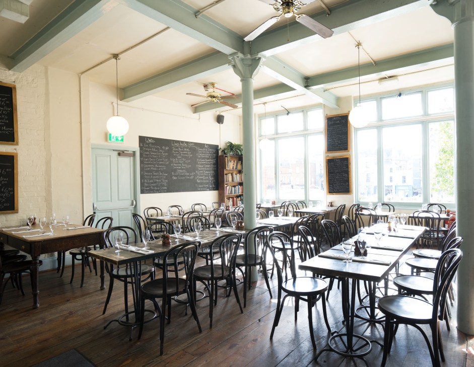 The Winding Stair restaurant interior with black bentwood chairs, white tablecloths, large windows, and bookshelves.