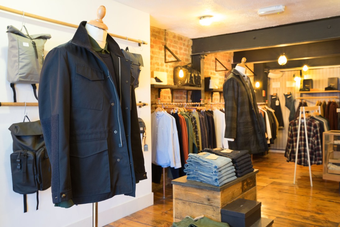 Interior of Indigo & Cloth clothing boutique with mannequins displaying navy jackets and organized merchandise under warm lighting.