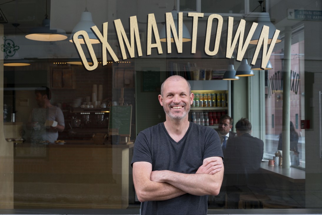 Man standing in front of Oxmantown café storefront with illuminated signage.
