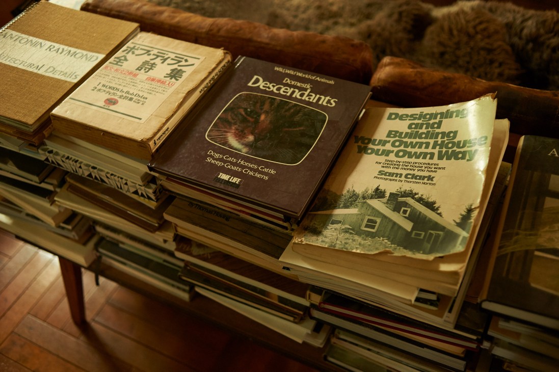 A collection of hardcover books stacked on a wooden shelf, including titles about design and building.