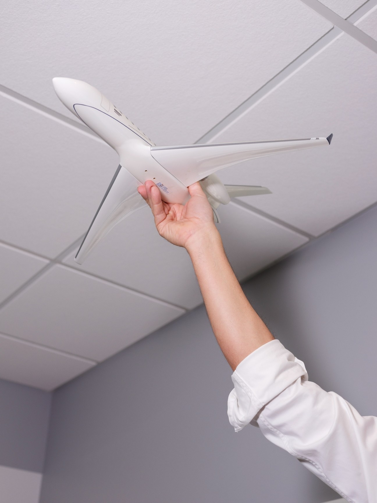 Hand holding a white airplane model against a ceiling.