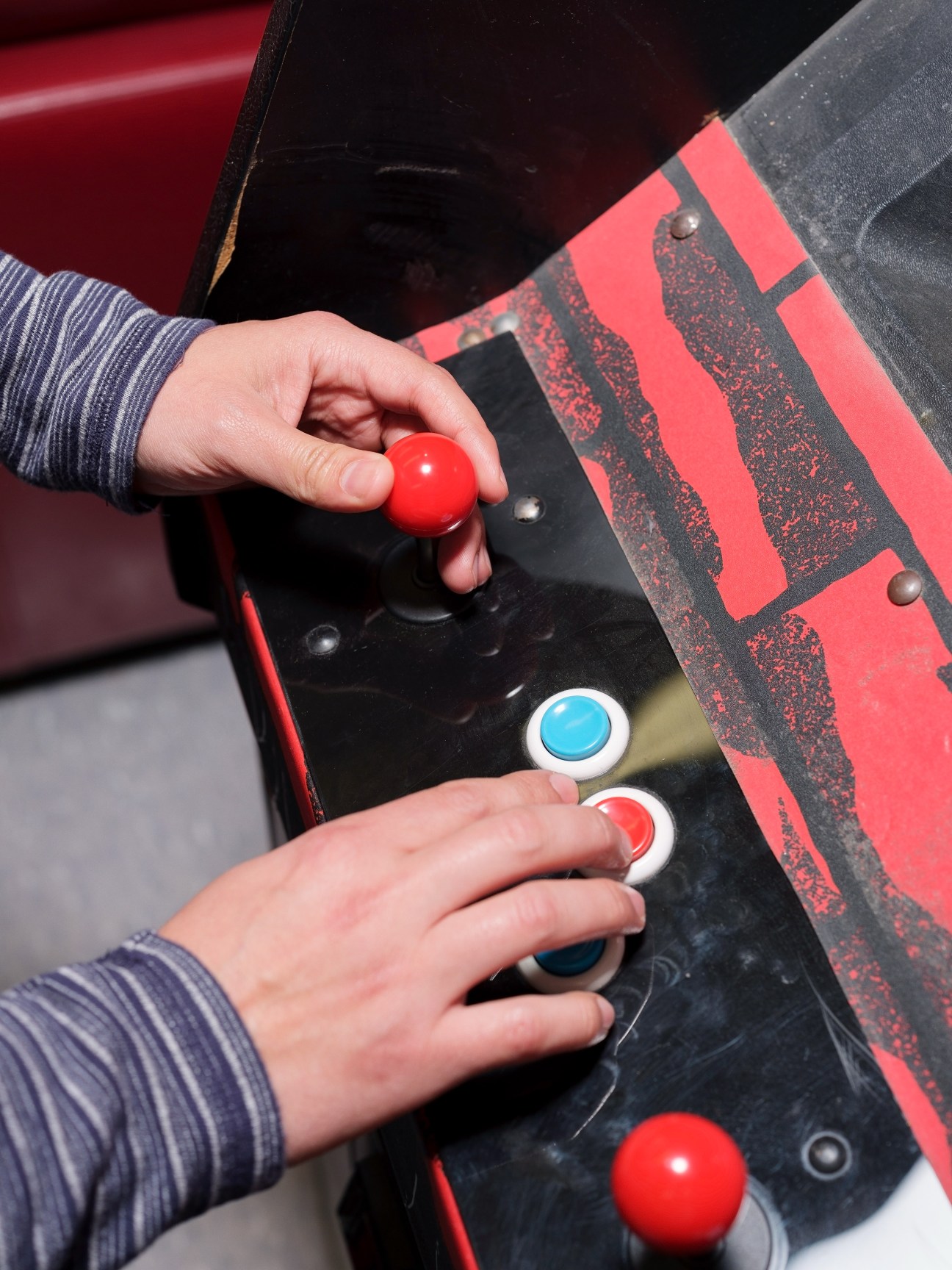 Hands playing a vintage Pac-Man arcade machine with red and blue buttons.