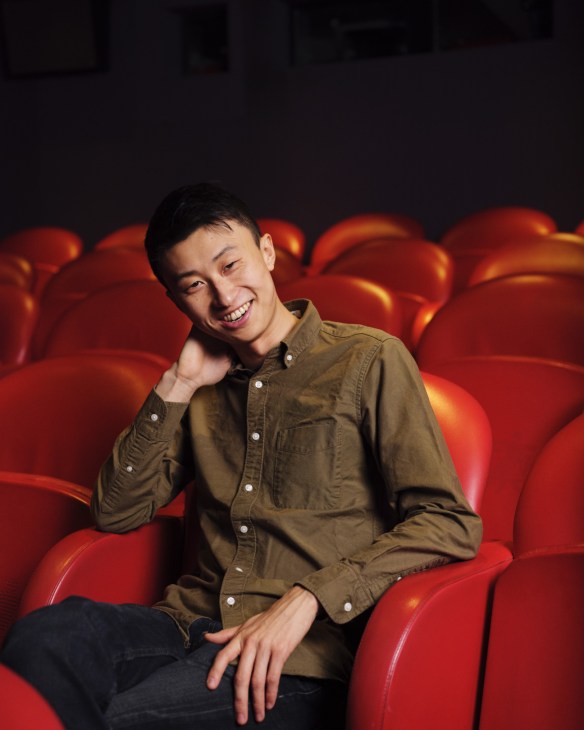 Filmmaker Bing Liu sits smiling on red cinema seats.