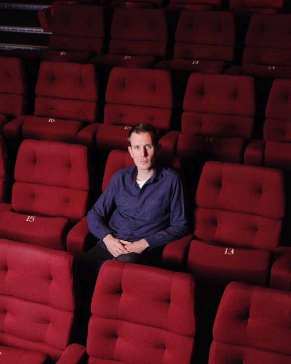 James Jones, a UK documentary filmmaker, sits among red cinema seats at a screening room.