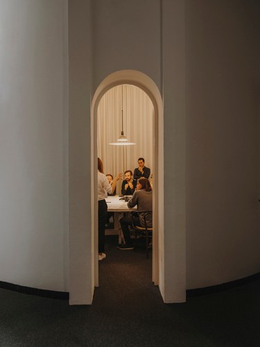 People in meeting pods inside an office with arched doorway and wooden interior structure.