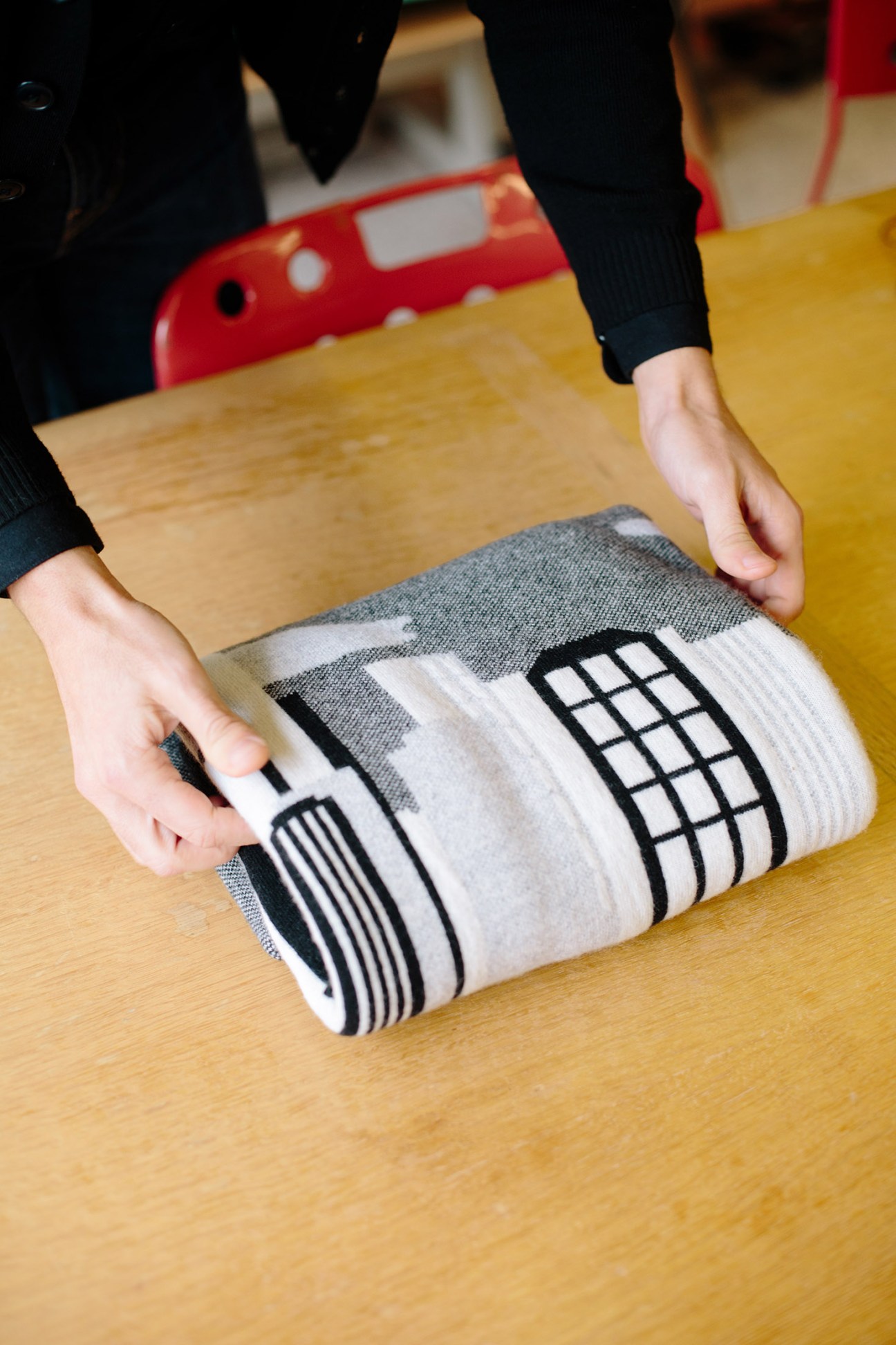 Person holding a rolled textile with geometric black and white pattern on wooden table.