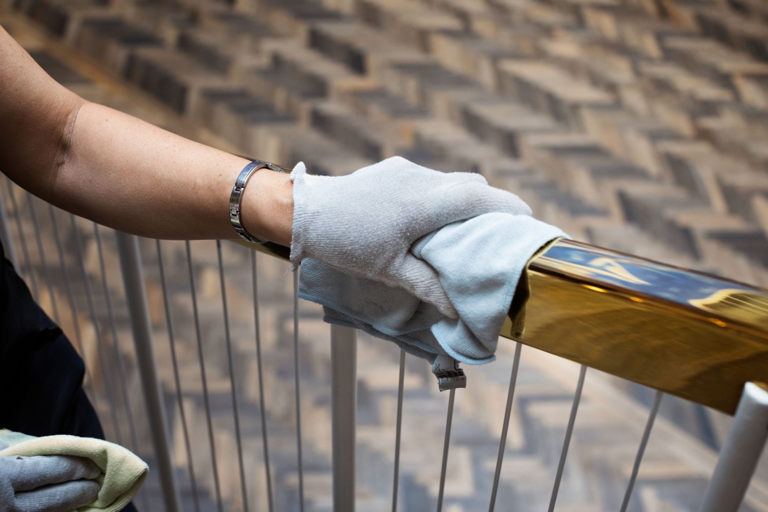 A hand wearing white gloves polishes a brass railing with a cloth.
