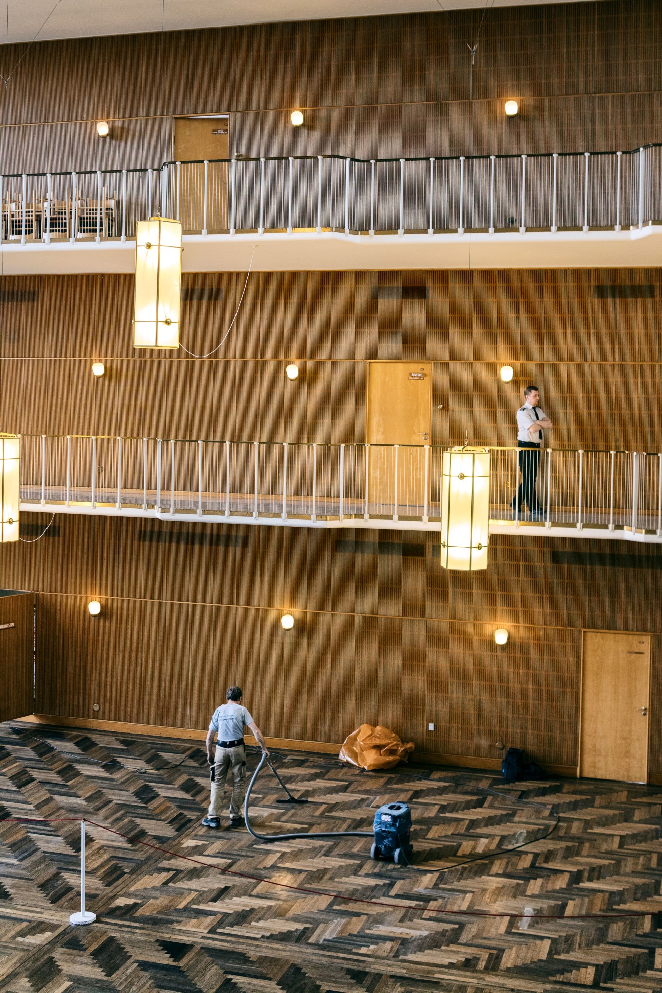 Worker cleaning the herringbone parquet floor in Aarhus city hall's main atrium with timber-lined balconies.