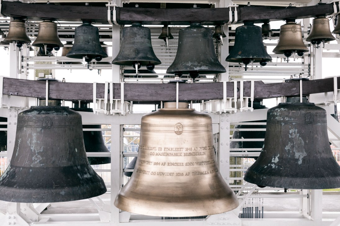Refurbished bells hanging in the Aarhus city hall clock tower, including a newly cast brass bell in the center surrounded by darkened older bells.