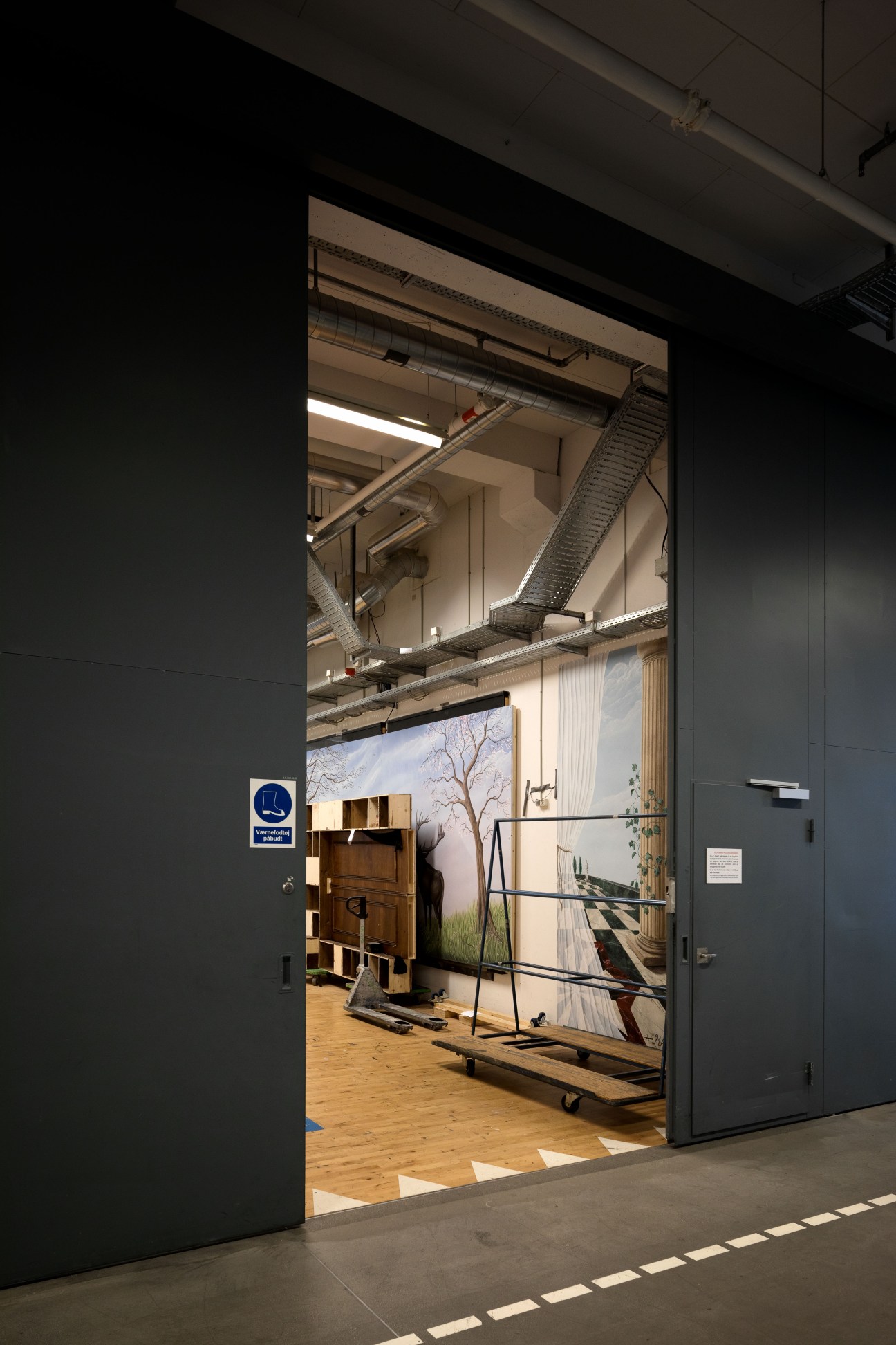 DR soundstage interior with wooden flooring, industrial lighting, set pieces and props visible through open doorway.