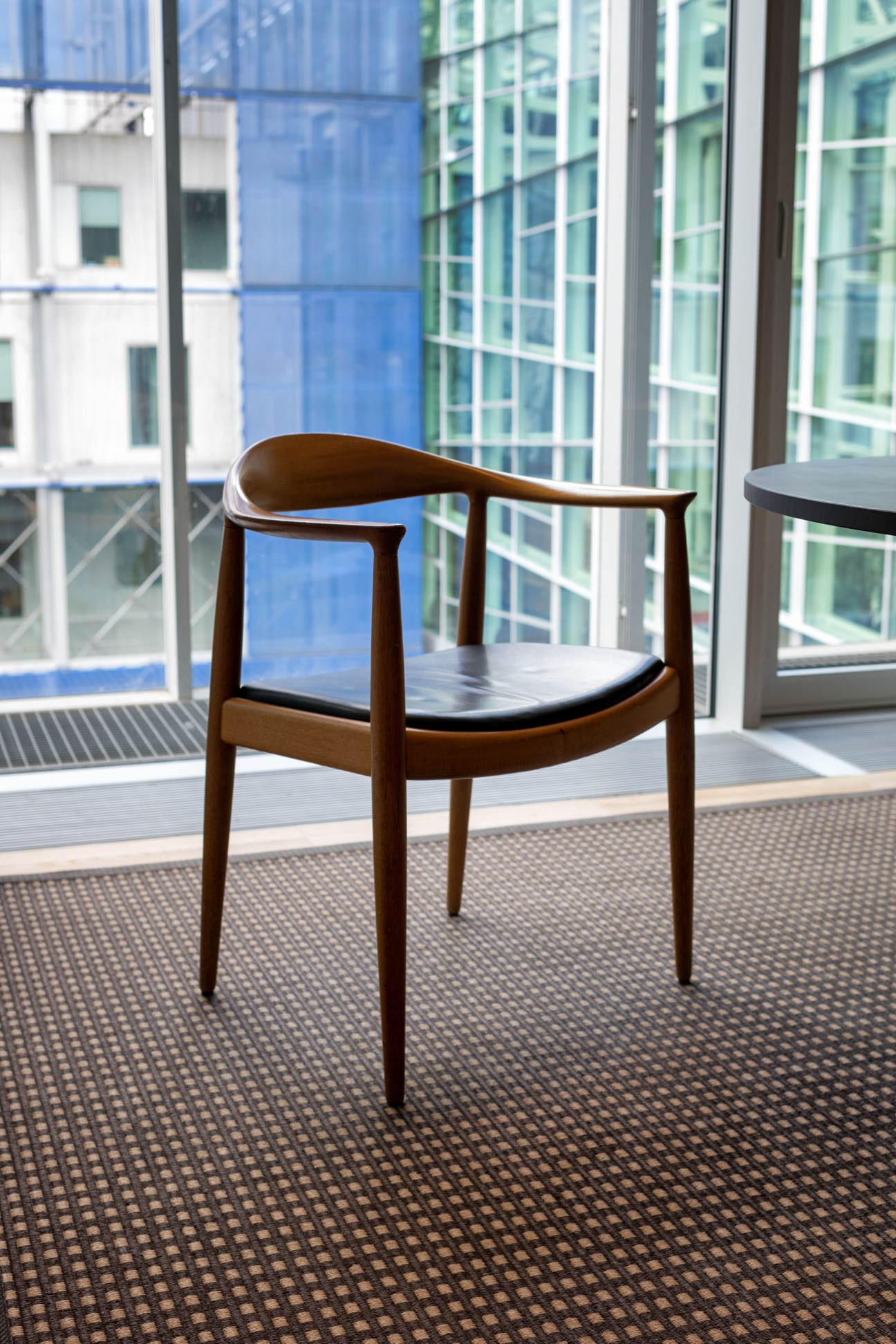 Hans J Wegner's The Chair - a wooden mid-century modern armchair with black seat cushion by a window overlooking Copenhagen.