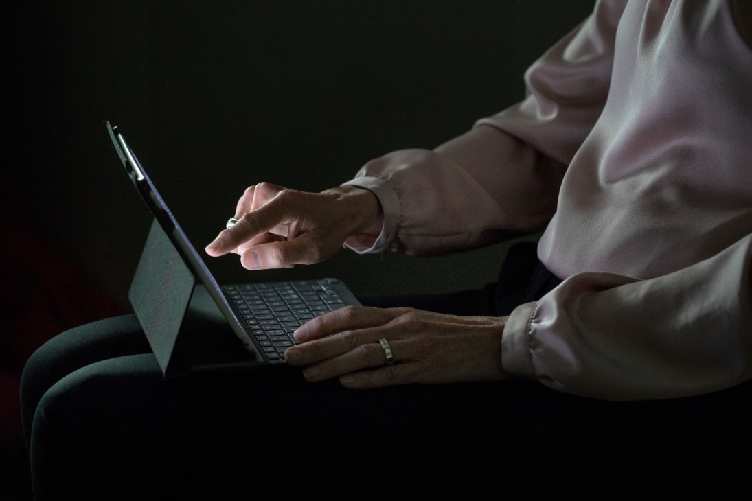 Hands holding and using an iPad tablet device against a dark background.