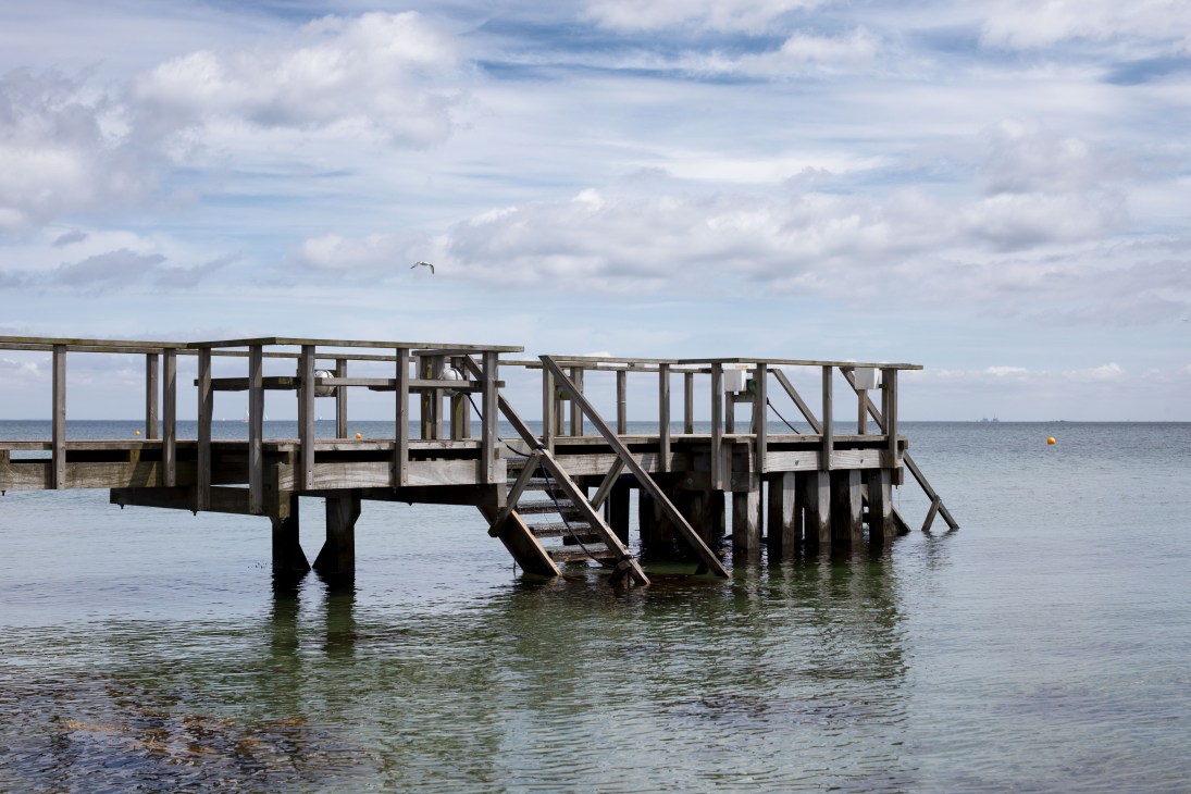 Wooden pier structure extending into calm sea under cloudy sky in Harboøre, Denmark.