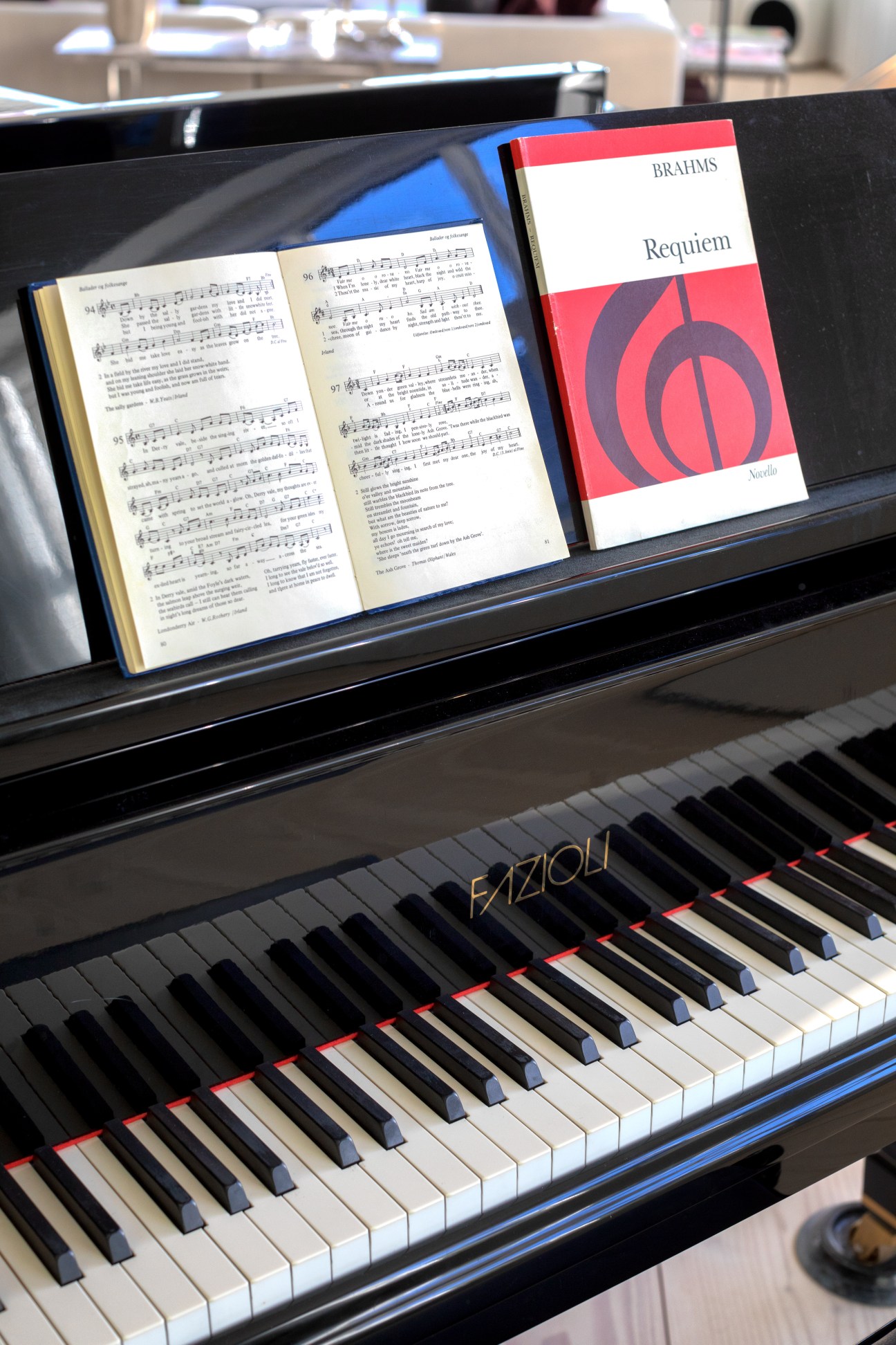 Piano keyboard with sheet music and Brahms Requiem score displayed on music stand.