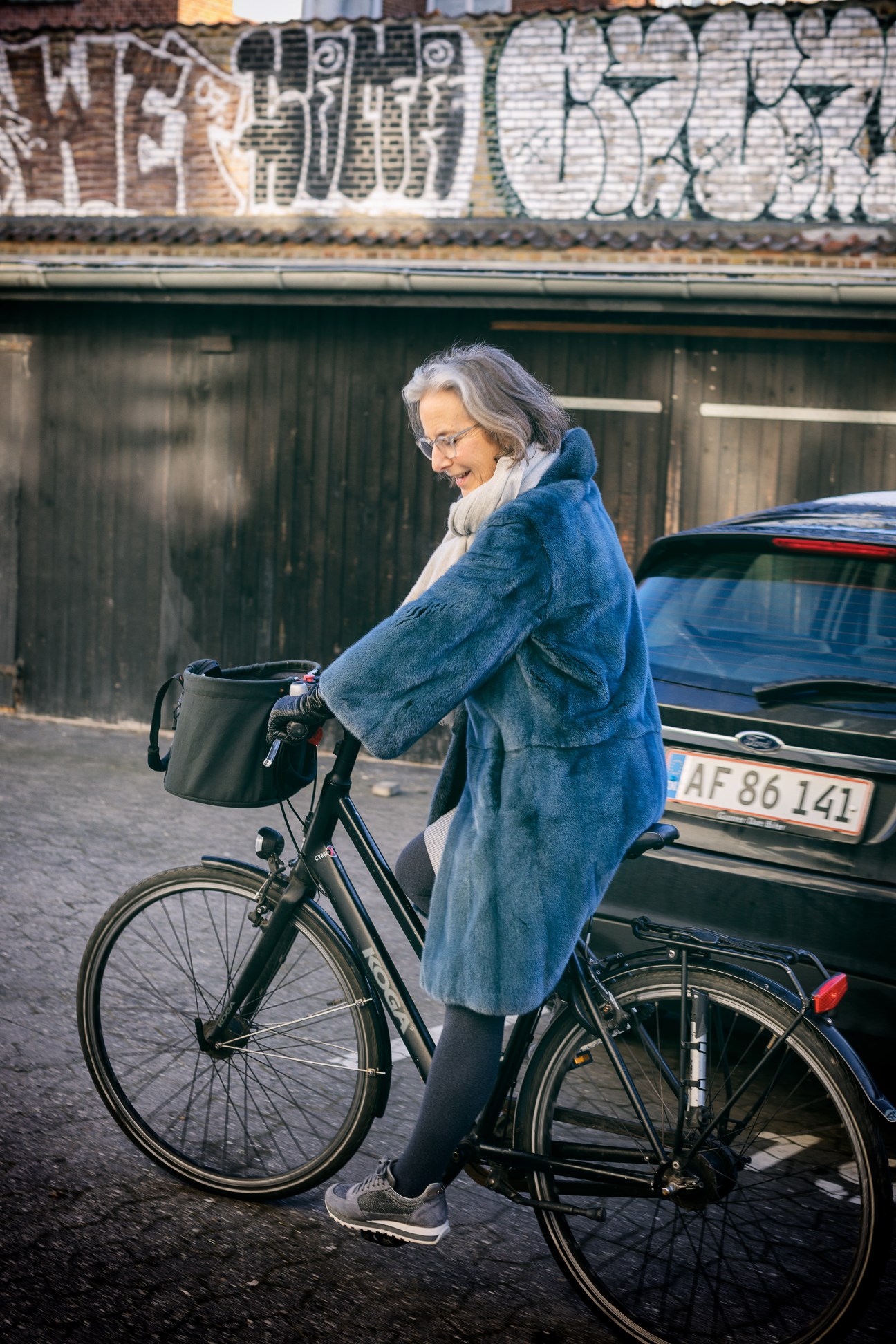 Jette Egelund rides a bicycle with a basket in Copenhagen, wearing a blue denim jacket.