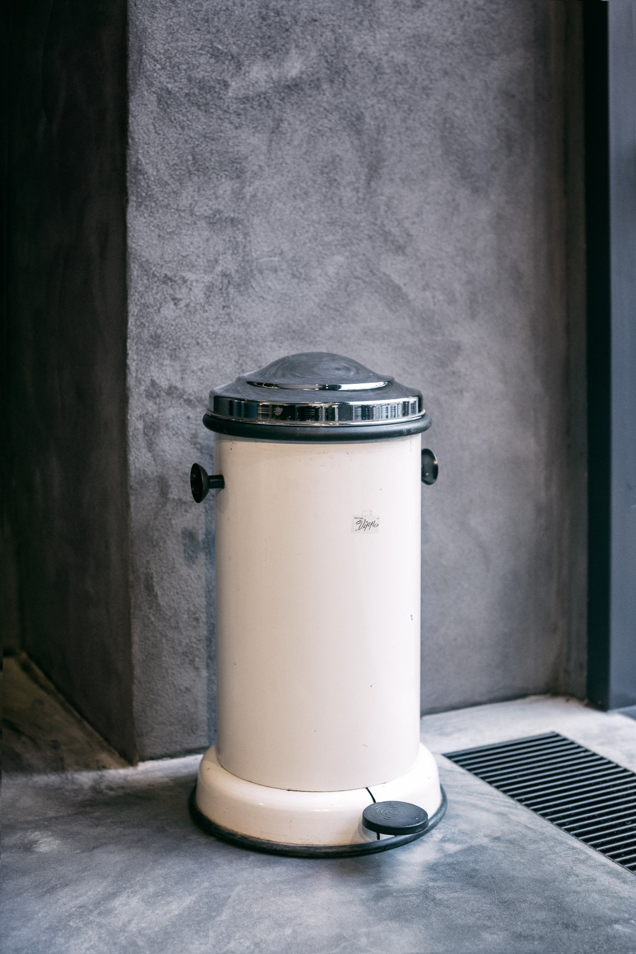 Vintage cream-colored Vipp pedal bin with chrome lid and black foot pedal on concrete surface.