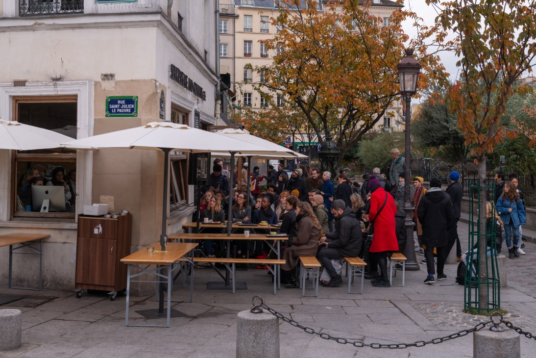 Outdoor café seating with large crowd gathered around tables and standing near Shakespeare and Company Café on a cold Paris morning.