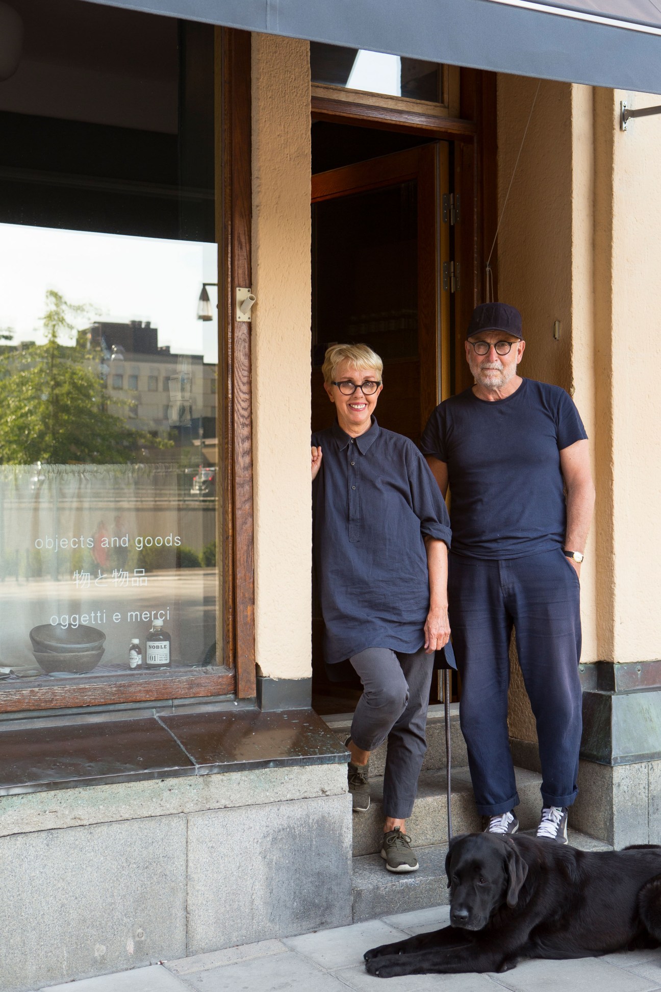 Enzo and Kersti Bussoli stand outside Objects and Goods shop in Stockholm with their black dog.
