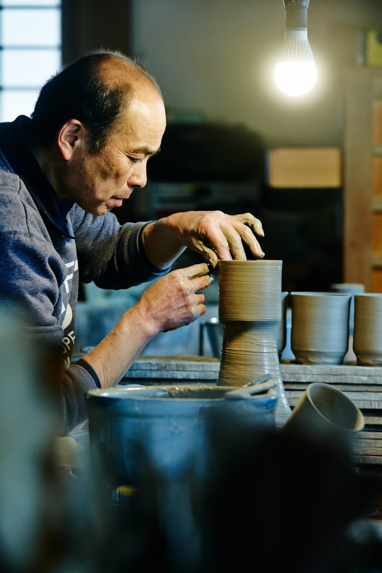 Craftsman working on hand-thrown ceramic vessel under warm light in pottery studio.