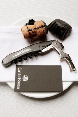 Ca' del Bosco business cards and wine corkscrew arranged on white surface.