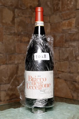 A bottle of Barbera wine wrapped in plastic with a label visible against a stone background.