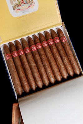 An open box of Cuban cigars with red and gold bands arranged in rows.