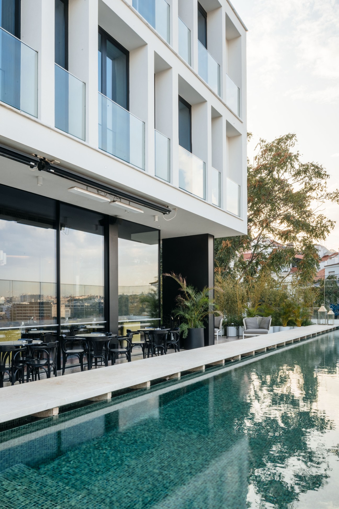 Modern hotel building with pool, terrace seating, and city views overlooking Lisbon