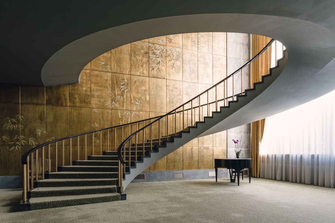 Modern spiral staircase with curved concrete ceiling, wood paneling, and metal railings in Hotel Ritz Lisbon.