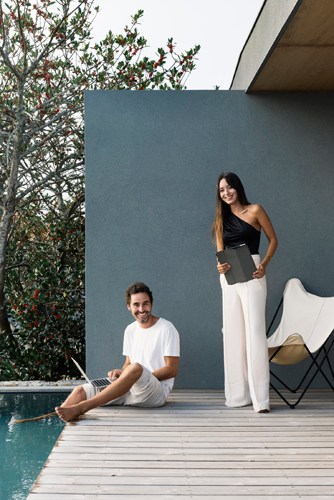 Two people relax by a swimming pool on a modern office terrace with grey wall and wooden deck.