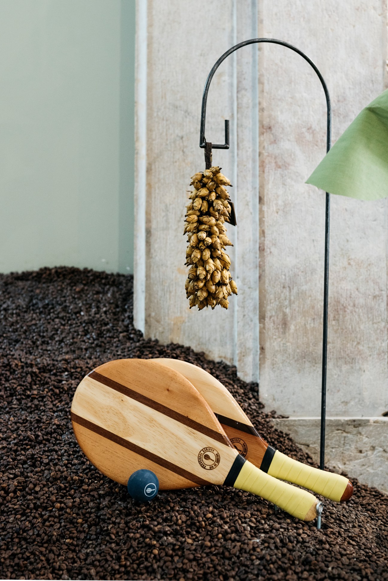Frescobal Carioca wooden paddles and ball displayed with dried hops and plant in minimalist setting.