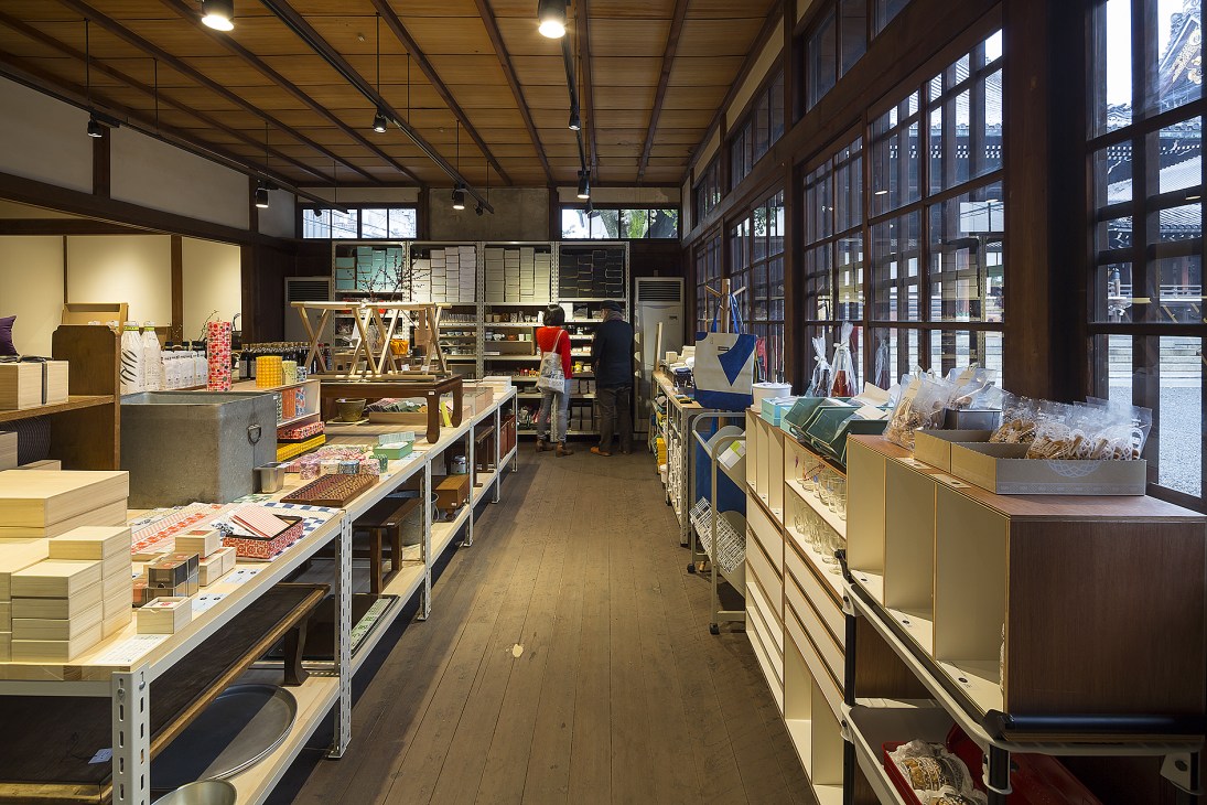 Interior of D&Department Kyoto shop displaying homeware, food, and craft items on shelves and tables.