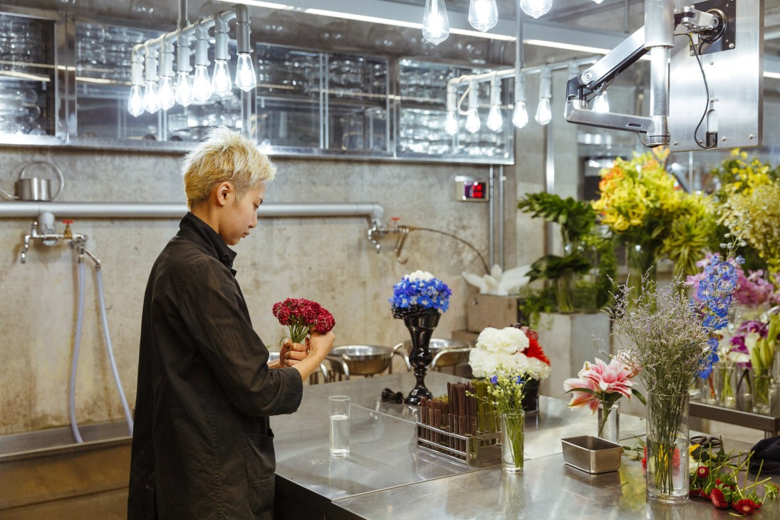 Florist arranging red carnations in a minimalist white flower shop interior.