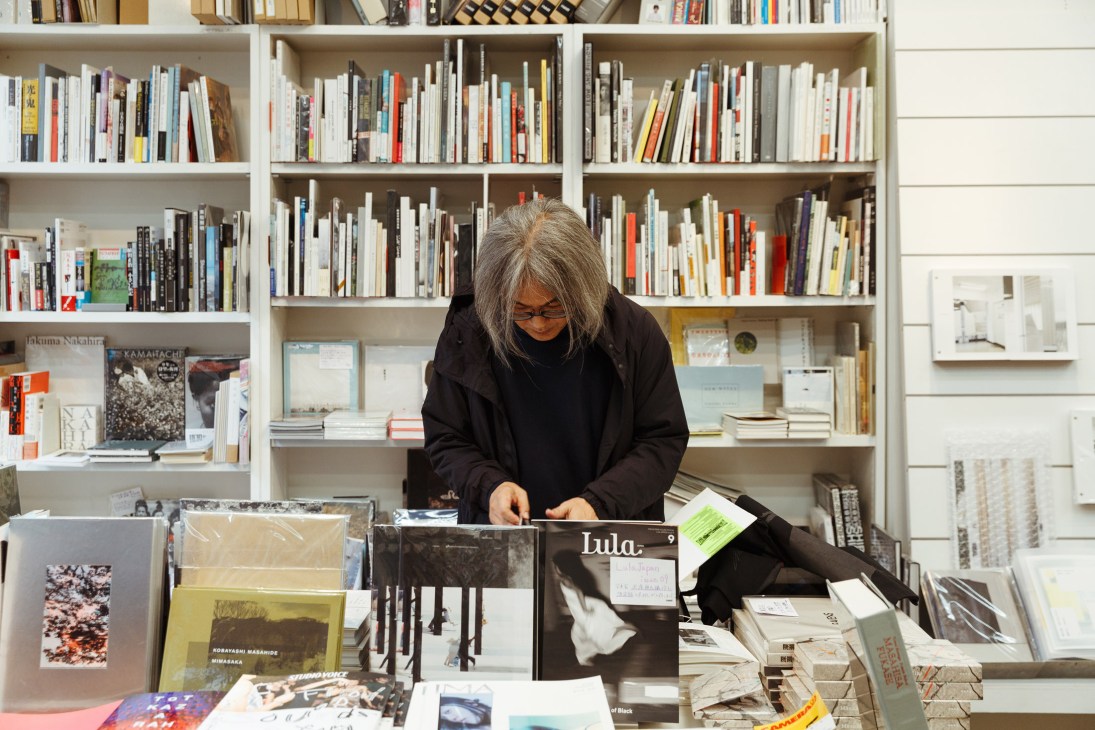 Woman browsing art books and prints at Nadiff bookshop with shelves of books and gallery items behind her.