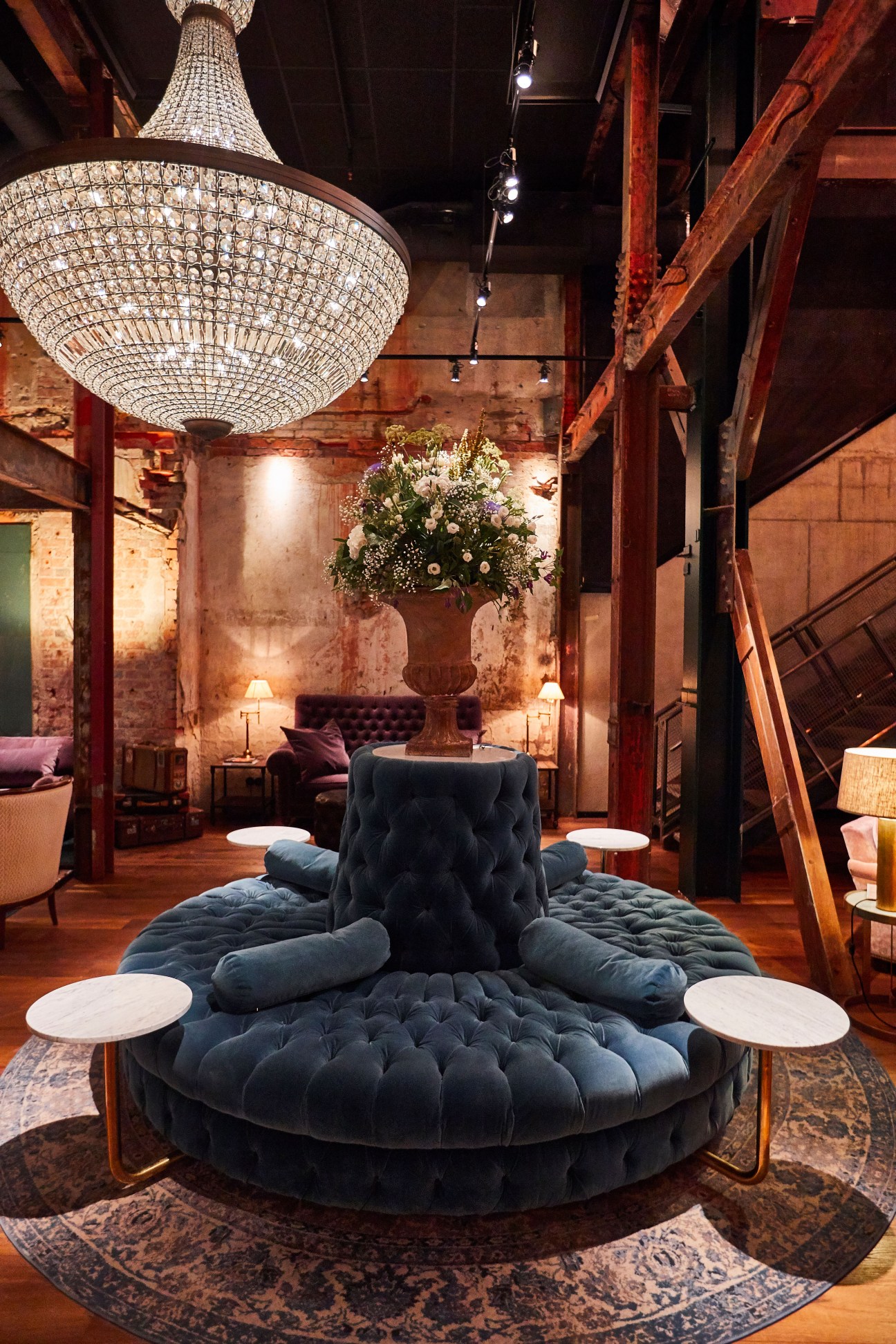 The Steam Hotel lobby in Västerås featuring a grand crystal chandelier, exposed red brick walls, and a blue velvet seating installation.