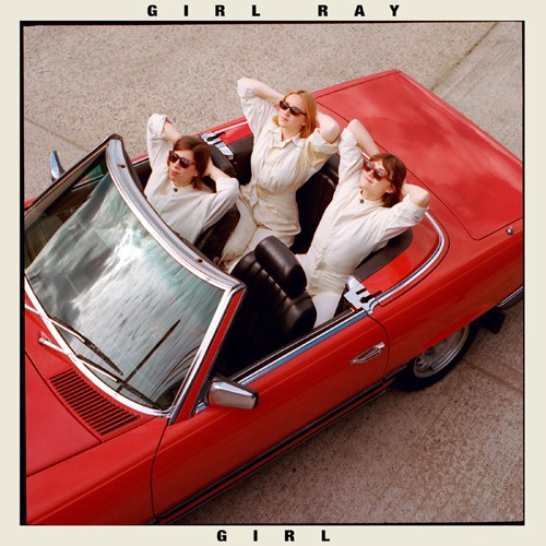 Three women in white shirts and sunglasses in a red convertible car viewed from above.