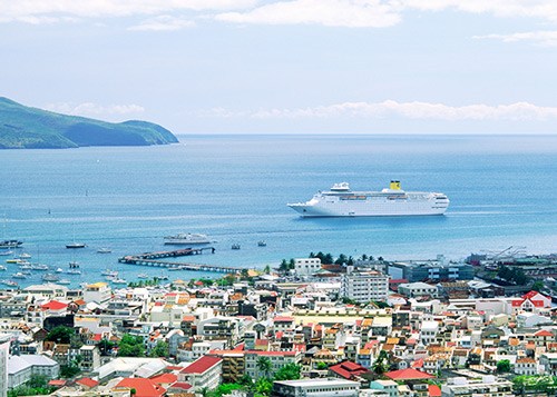 Cruise ship anchored off a colorful coastal town with residential buildings and mountains in the background.