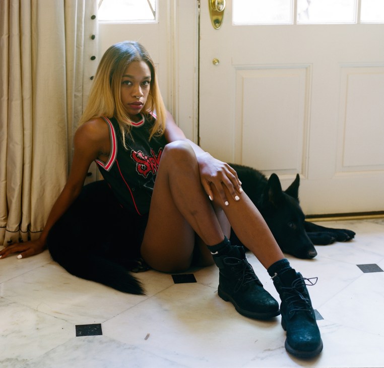 Portrait of musician Abra sitting on a floor wearing a black tank top and boots