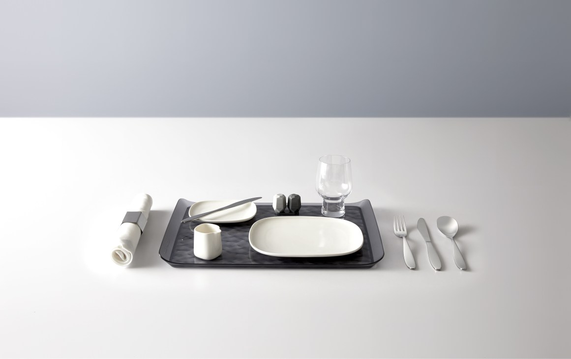 Delta Air Lines tableware set by Alessi featuring plates, glasses, cutlery and accessories arranged on a black placemat.
