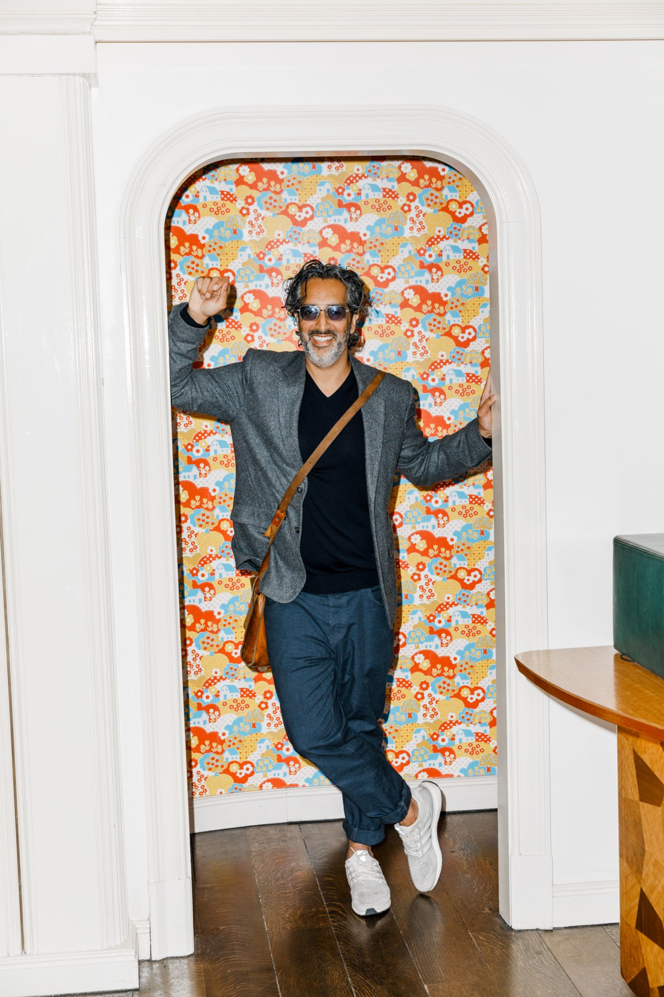 Amar Lalvani, CEO of Standard International, gestures enthusiastically in a doorway with colorful patterned wallpaper.