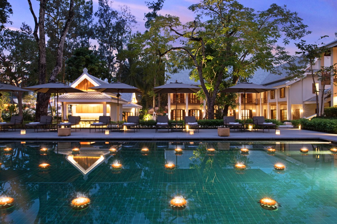 Azerai Luang Prabang hotel pool at dusk with illuminated loungers and colonial architecture reflected in water.