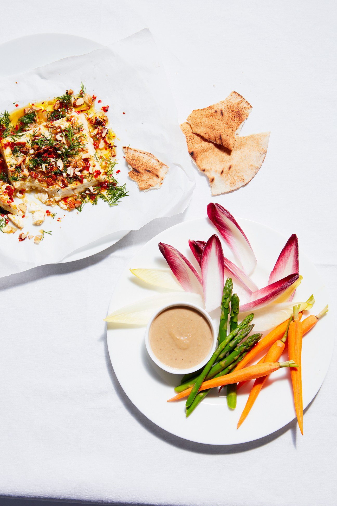 Bagna cauda anchovy and garlic dip in white bowl surrounded by fresh vegetables and flatbread on white plate.