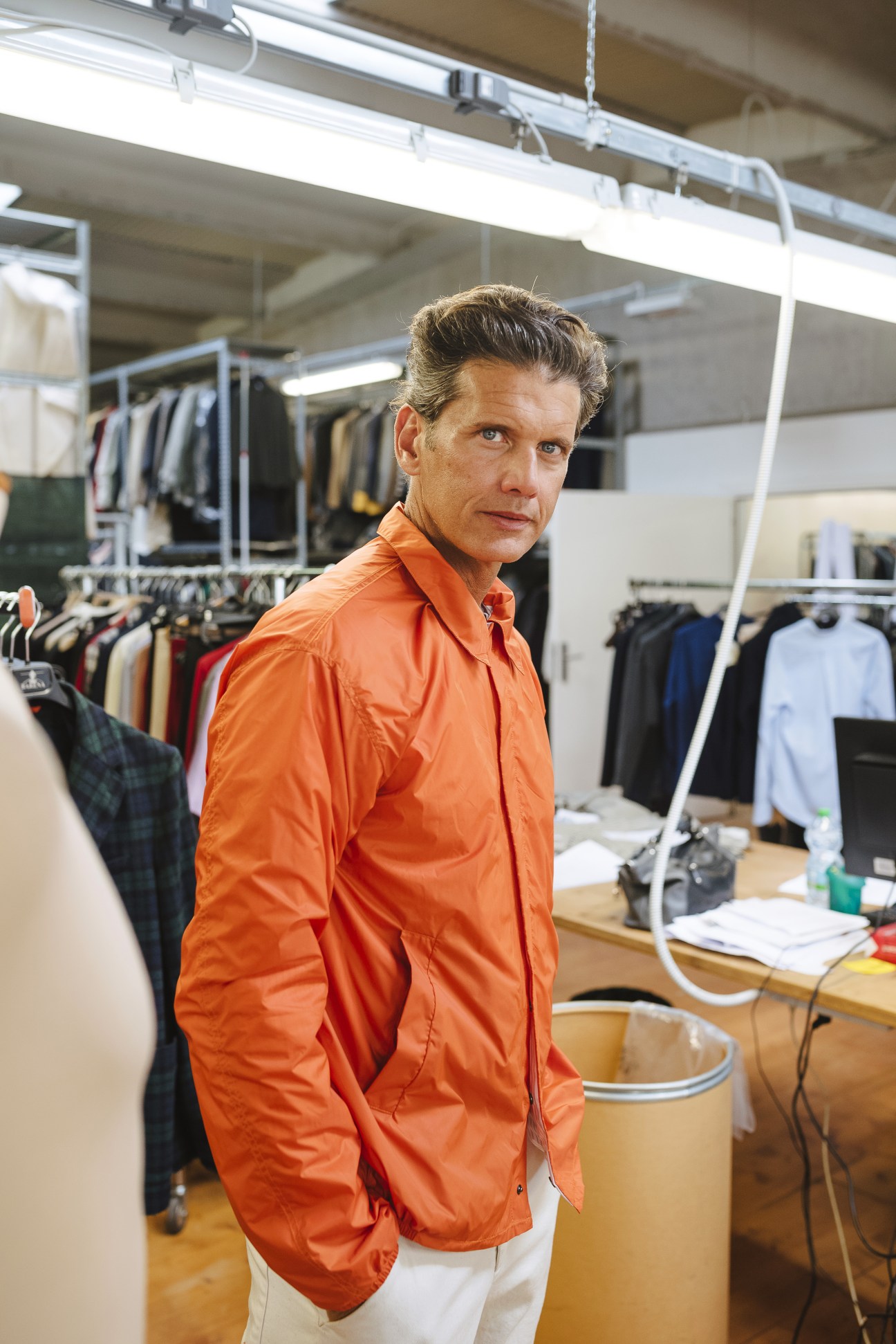 Pierfilippo Ligotti, an in-house model at Barena, stands in the studio wearing an orange shirt.