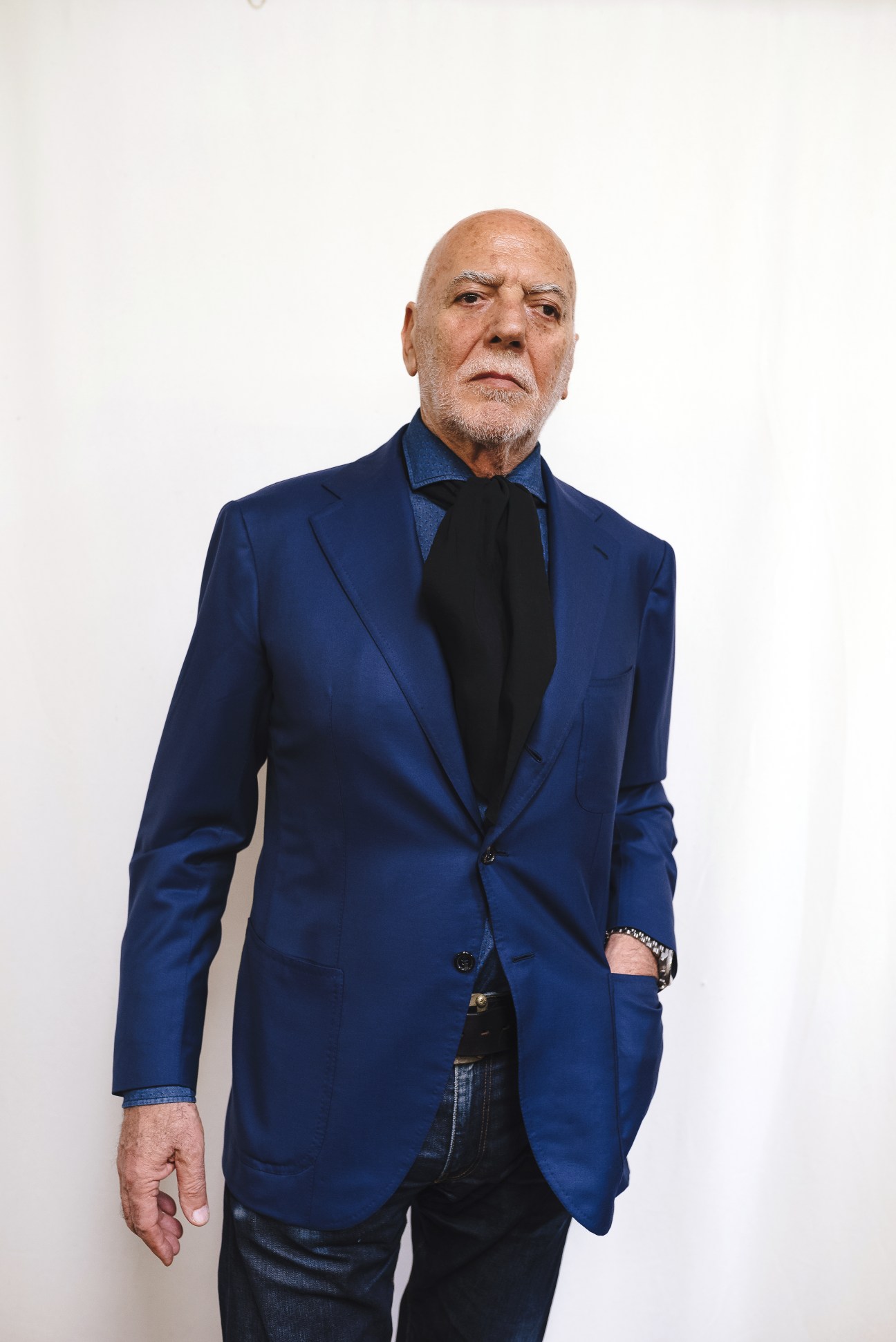 Portrait of Sandro Zara wearing a navy blazer and black scarf against a white background.